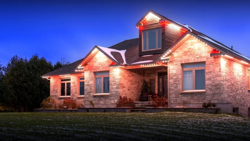Stone home lit in red and white permanent outdoor lighting at dusk