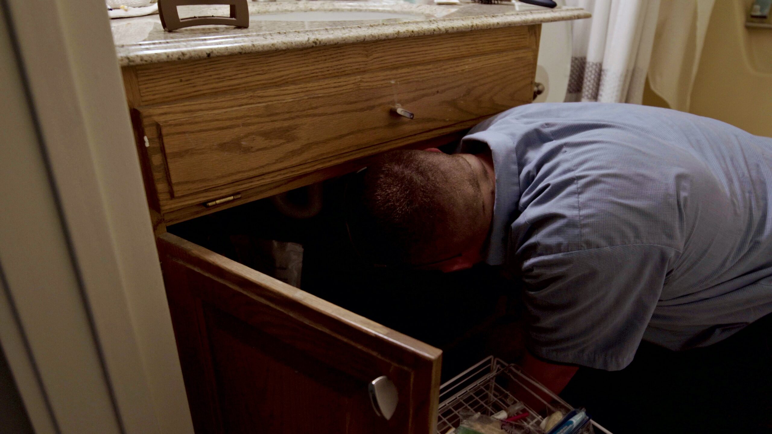 Paschal technician closing a shut-off valve under a sink while tracing a water leak in a Bentonville home